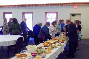 Buffet table with food and people serving themselves.