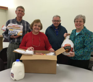 four people stand behind a large cardboard box containing food